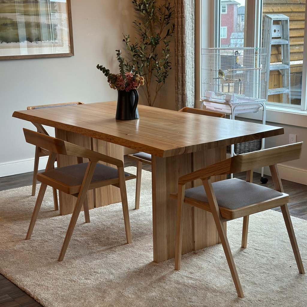 Wooden dining table with chairs in a room with large windows.
