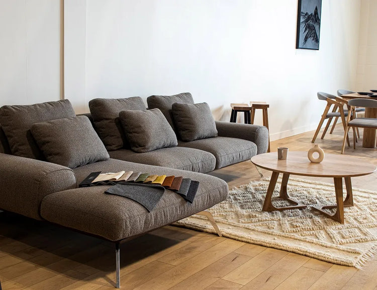 Grey sectional sofa with fabric swatches on the chaise, next to a round wood coffee table in a living room