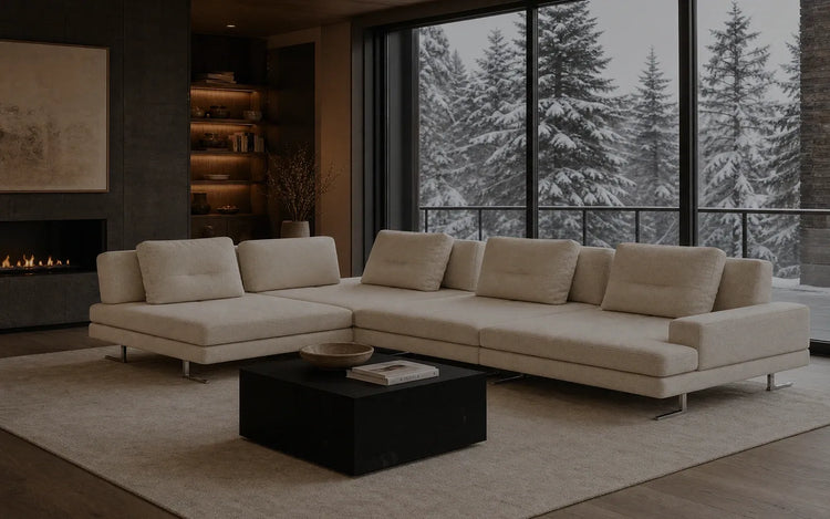 A spacious cream-coloured modular sectional sofa by Verdant Furniture in a cozy living room with a modern fireplace and a scenic window view of a Canadian snowy forest.