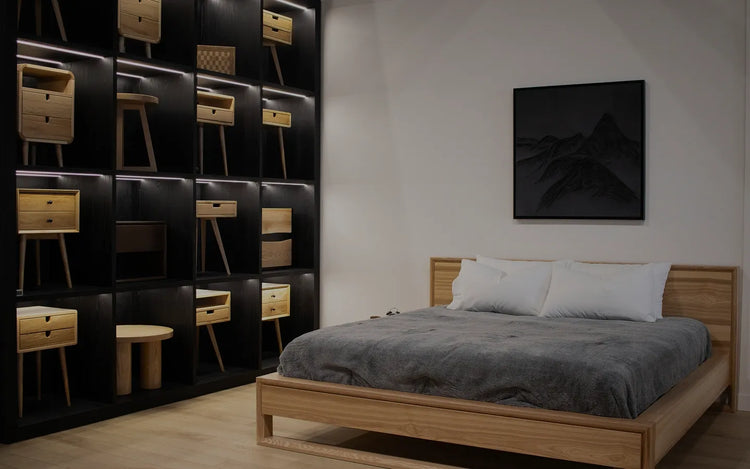 Wooden platform bed in a bedroom, with nightstand furniture displayed on lit shelving to the side